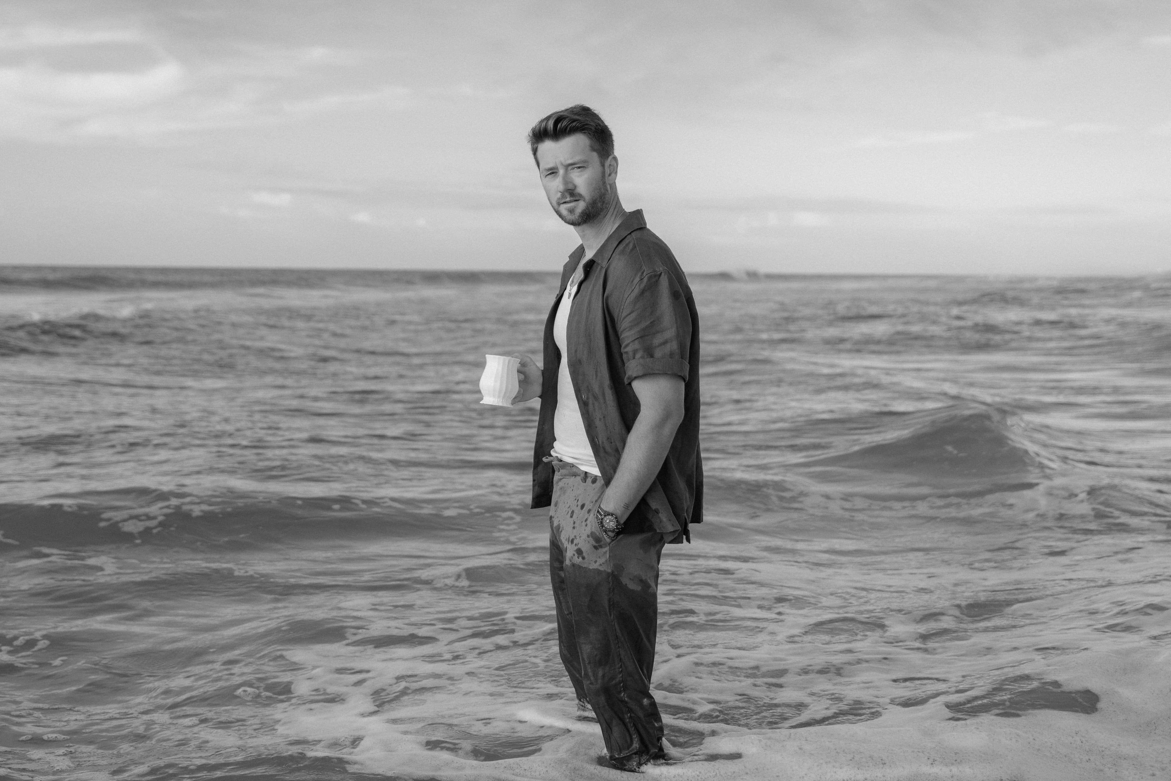 Adam Doleac standing in the ocean holding a cup, closing image for the 3 Minute Summer campaign
